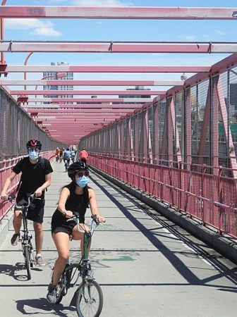 Looking east at bikers on Williamsburg Bridge on a sunny midday 13 June 2020
